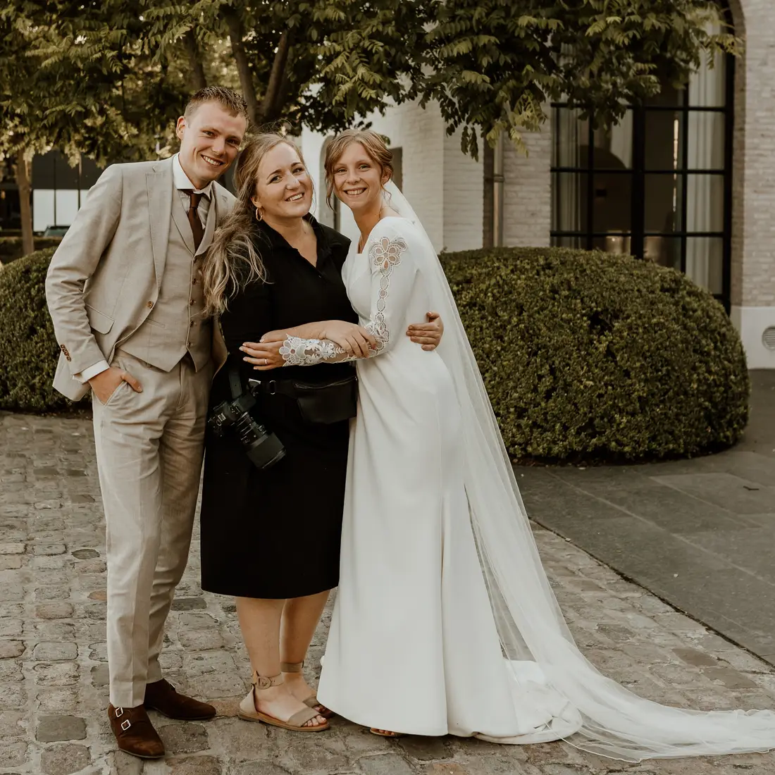 Bruidsfotograaf Marilyn Hansum met camera naast een bruidspaar